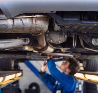 Technician in blue uniform underneath vehicle repairing transmission.